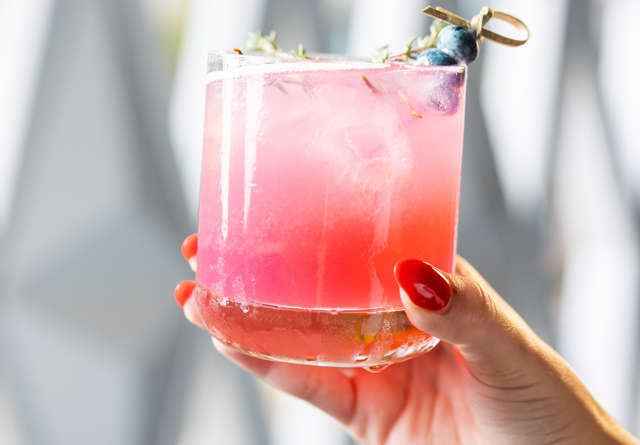 Refreshing pink cocktail garnished with blueberries, held in hand with a stylish manicure, perfect for a summer drink.