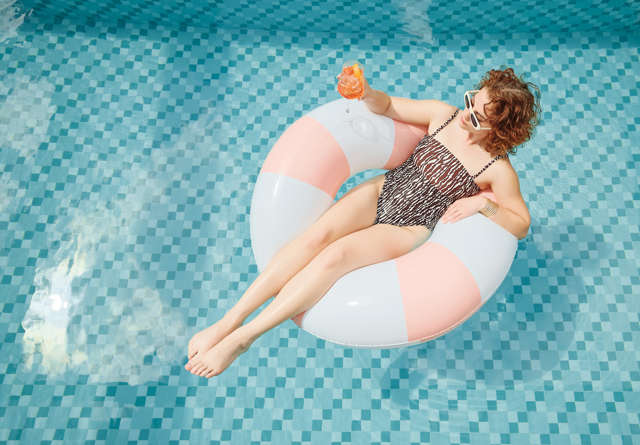 Guest relaxing on a pink and white float in the Virgin Hotels pool, holding a cocktail and enjoying the sun.