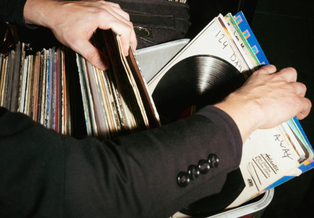 Person browsing through a vinyl record collection, selecting albums in a crate at Virgin Hotels.