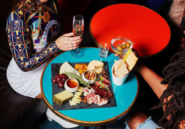Two people enjoying drinks and a charcuterie board at a cosy rooftop setting with a relaxed atmosphere.