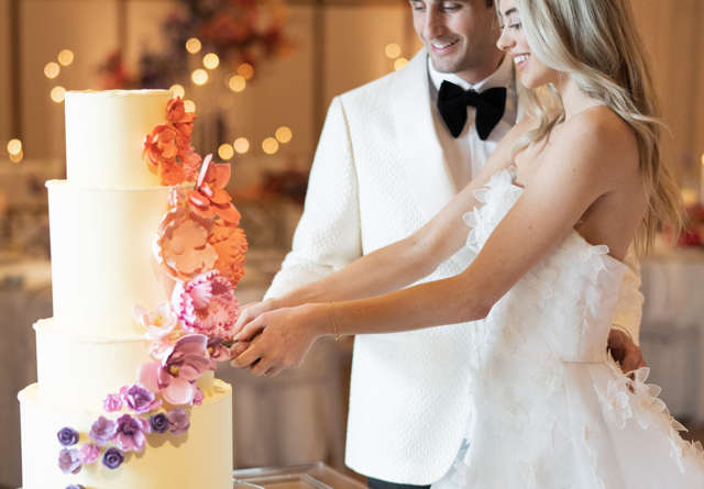 Bride and groom dressed elegantly whilst cutting an ornately decorated cake.